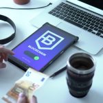 Tablet exibindo uma transação de moeda digital ao lado de um laptop e cédulas de euro.