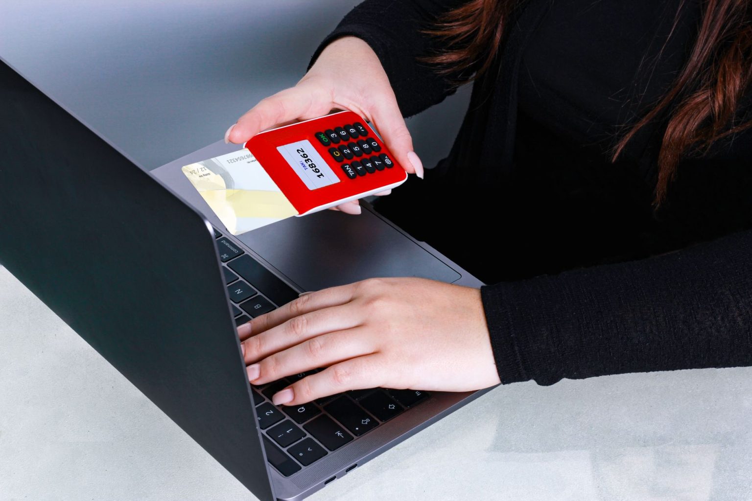 Mãos usando um cartão de crédito durante um pagamento online em um laptop.