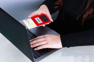 Mãos usando um cartão de crédito durante um pagamento online em um laptop.