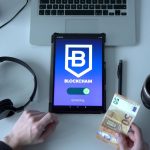 Tablet exibindo um aplicativo de blockchain ao lado de cédulas e ferramentas tecnológicas sobre uma mesa.
