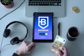 Tablet exibindo um aplicativo de blockchain ao lado de cédulas e ferramentas tecnológicas sobre uma mesa.