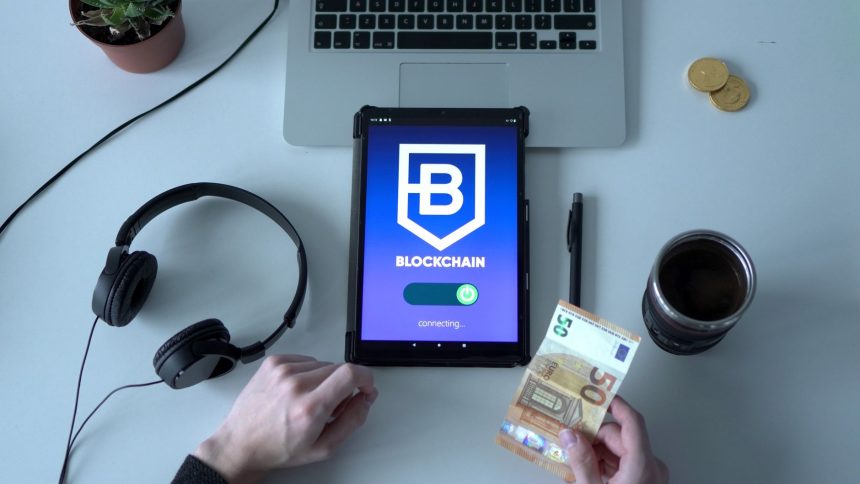 Tablet exibindo um aplicativo de blockchain ao lado de cédulas e ferramentas tecnológicas sobre uma mesa.