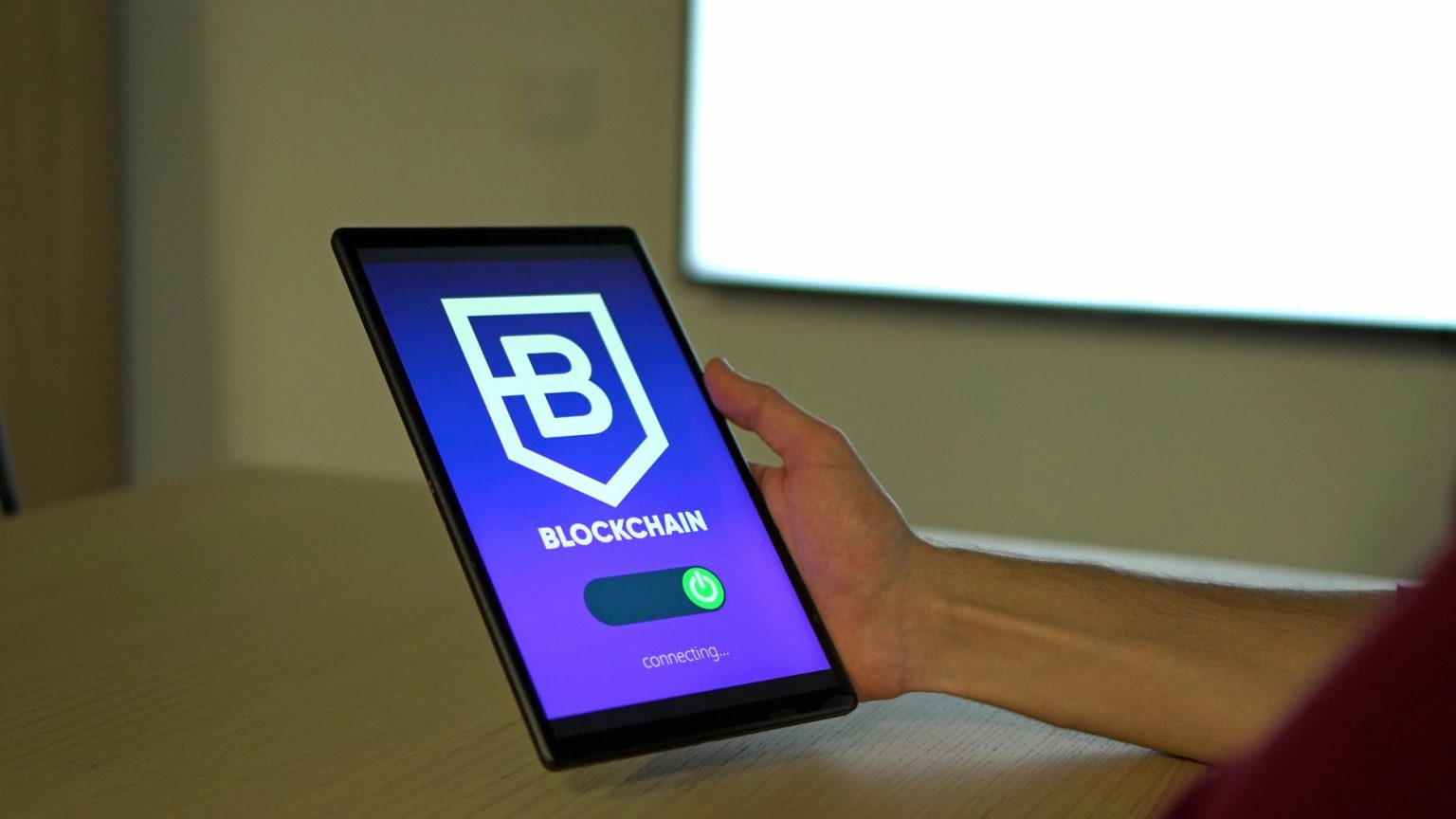 Mão segurando um tablet com uma representação de conexões de blockchain na tela.