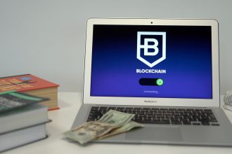 Laptop exibindo uma interface de conexão blockchain sobre uma mesa, ao lado de livros e cédulas de dólar.