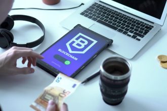 Tablet exibindo uma transação de moeda digital ao lado de um laptop e cédulas de euro.