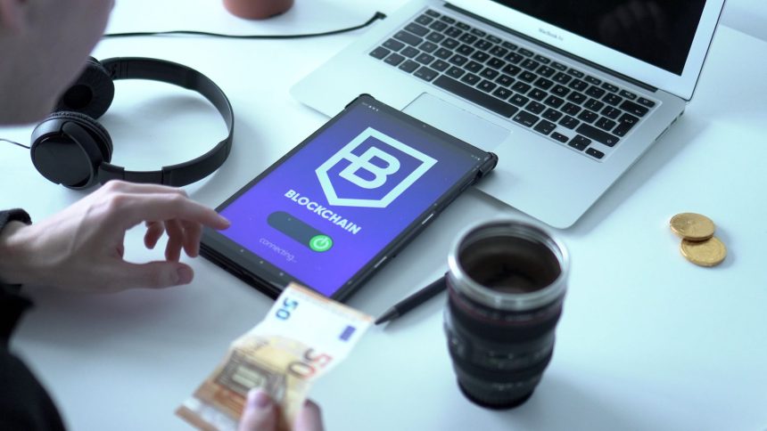 Tablet exibindo uma transação de moeda digital ao lado de um laptop e cédulas de euro.