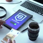 Tablet exibindo uma transação de moeda digital ao lado de um laptop e cédulas de euro.